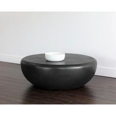 a white bowl sitting on top of a black ottoman in front of a white wall