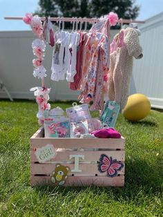 a wooden crate filled with baby items on top of a grass covered field next to a teddy bear