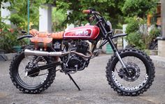 a red and black dirt bike parked on top of a parking lot next to trees