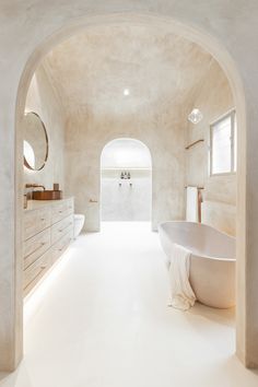 a large white bathroom with an arched doorway leading to the bathtub and sink area