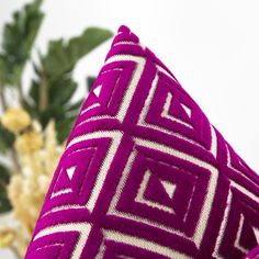 a purple and white pillow sitting on top of a table next to a vase with flowers