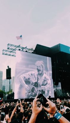 the crowd is taking pictures with their cell phones at an outdoor music festival in front of a large screen