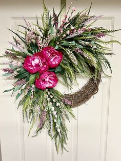 a wreath with pink flowers and greenery hanging on a door