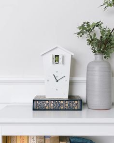 a white clock sitting on top of a book shelf next to a vase filled with flowers