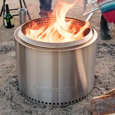 a person standing next to a large pot on top of a fire pit in the dirt