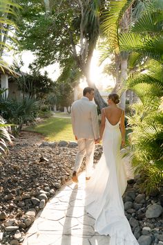 a bride and groom walking down a path in front of palm trees on their wedding day