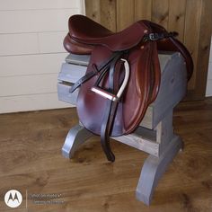 a brown horse saddle sitting on top of a wooden bench