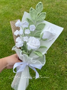 a hand holding a bouquet of flowers on top of a grass covered field in the daytime