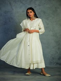 Chanderi kurta in Off White with mirror work on yoke and sleeves. This Front yoke gathered kurta set is paired with a chanderi dupatta with mirror work on borders and comes along with cotton flared palazos highlighted with mirrors.Perfect festive dressing for a glittery evening. Color: Off White Fabric: Kurta- Chanderi Dupatta - Chanderi Palazzo - Cotton Lining - Cotton Note: Available in other colors The product will be delivered within 2-4 weeks of order placed Wash Care - Dry clean only Hand White Kurta, Sustainable Clothing Brands, Indian Fashion Designers, Mirror Work, Festival Dress, White Embroidery, Kurta Set, Off White Color, Palazzo Pants