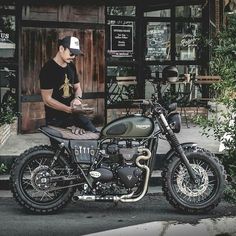 a man sitting on top of a motorcycle parked in front of a building next to trees