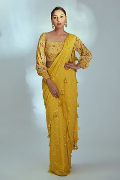 Yellow pre-draped saree with mirror embroidery and tassel details. Comes with smocked blouse with floral patterns.
Component: 2
Pattern: Printed, Embroidered
Type Of Work: Floral Pattern, Mirror Work
Neckline: Square
Sleeve Type: Bishop Sleeves
Fabric: Crepe
Color: Yellow
Other Details: 
Pre draped saree
Fully shantoon lining
Smocked blouse
Tassel hem pallu
Note: Blouse can be worn as an off shoulder or with shoulders.
Occasion: Mehendi and Haldi - Aza Fashions Hand Flare, Flared Lehenga, Lehenga Pattern, Cotton Blouse Design, Draped Saree, Smocked Blouse, Mirror Embroidery, Floral Mirror, Purple Saree