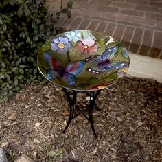 a glass bowl sitting on top of a metal stand next to a brick wall and shrubbery