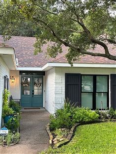 a white house with black shutters on the front door and green grass around it