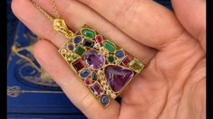 This gorgeous 18K yellow gold enhancer pendant is bezel set with six (6) natural blue sapphires, two (2) natural peridot, two (2) natural emeralds, two (2) natural jadeite jade, two (2) natural pink sapphires, two (2) natural purple sapphires, two (2) natural amethyst and eleven (11) round brilliant cut diamonds. The tapered bail is bead set with two (2) round brilliant cut diamonds. The pendant measures 48.00mm X 31.00mm and is suspended from a 14K yellow gold neck chain measuring 18 inches in length. One of the peridots is lightly chipped. Yellow Gold Multi-stone Art Deco Jewelry, Art Deco Multi-stone Yellow Gold Jewelry, Art Deco Yellow Gold Multi-stone Jewelry, Fine Jewelry Cabochon Gemstone Pendant, Elegant Rectangular Multi-stone Jewelry, Elegant Multicolor Pendant Gemstones, Elegant Multicolor Gemstone Pendant, Art Deco Multicolor Jewelry For Gift, Multicolor Art Deco Jewelry For Gift