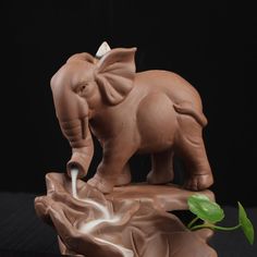 an elephant figurine is shown with a plant in the foreground and a black background