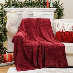 a red blanket sitting on top of a white couch next to a christmas tree and stockings