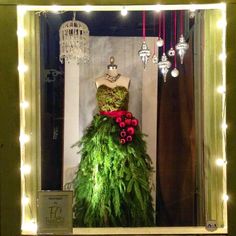 a dress made out of plants is displayed in a shop window with lights around it