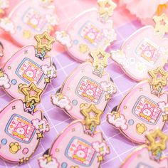 pink and gold hello kitty broochies are on a purple surface with flowers in the background