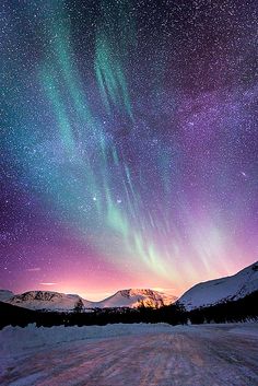 the sky is filled with stars and aurora lights above snow covered mountains in the distance