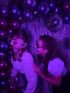 two women standing next to each other in front of purple and black balloons with disco balls behind them