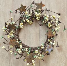 a wreath made out of metal stars and white flowers on a wooden surface with green leaves