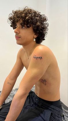 a shirtless man sitting on top of a bed next to a white wall with writing on his chest