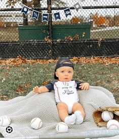 a baby is sitting on a blanket with baseballs and mitts in front of him