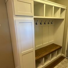 a wooden bench sitting in front of a white coat rack with hooks on it's sides