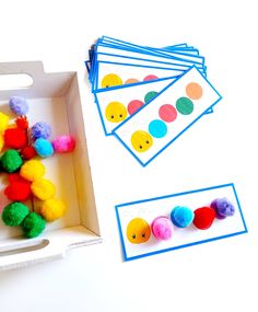 a box filled with pom - poms next to some cards and scissors on the table