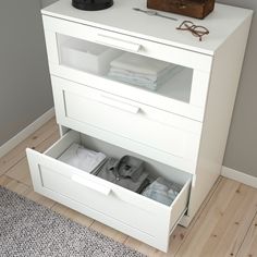 an open drawer with folded clothes in it on a wooden floor next to a wall