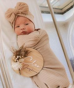 a baby wrapped up in a blanket with a name on it and a wooden sign