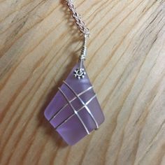 a necklace with a purple stone hanging from it's side on a wooden surface