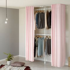 an open closet with pink curtains and clothes hanging on the racks, in front of a white wall