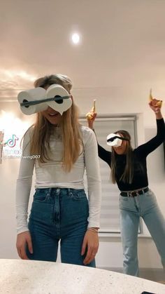 two young women wearing virtual glasses and holding up their hands in the air while standing next to each other