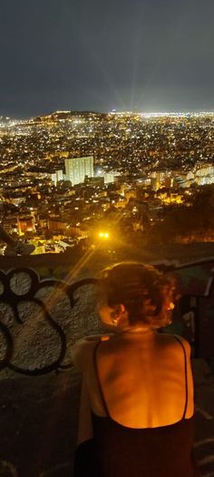 a woman sitting at the top of a hill looking down on a cityscape