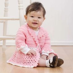 a baby sitting on the floor wearing a pink crochet sweater