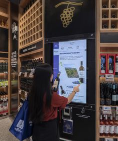 a woman standing in front of a vending machine with bottles of wine on it