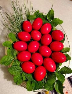 a bowl filled with lots of red eggs and green leaves on top of a table