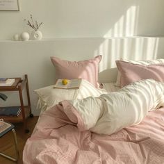 a bed with pink and white sheets, pillows and a book on the end table