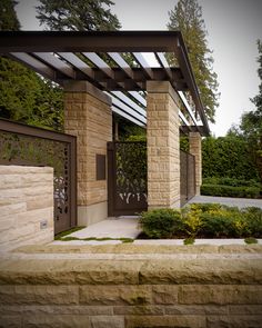 the entrance to a home with stone walls and plants on either side, along with a pergolated roof