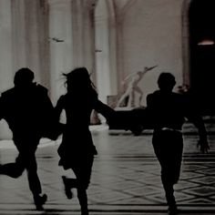 three people are running in the middle of a hall with their arms around each other