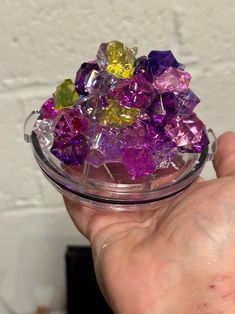 a hand holding a glass bowl filled with different colored rocks