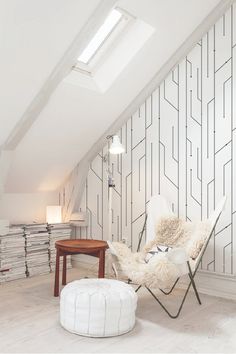 a chair and ottoman in an attic with white wallpaper, flooring and skylights