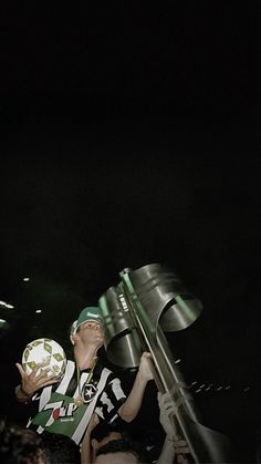 a man holding a soccer ball up to his face in front of a crowd at night