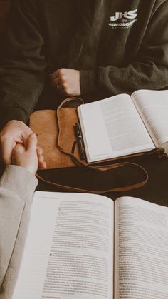 two people are sitting at a table with open books and one is holding the other's hand