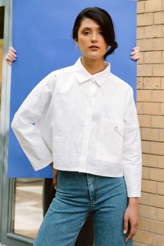 a woman standing in front of a brick wall wearing a white shirt and blue jeans