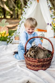 a little boy sitting on top of a bed next to a bunny in a basket