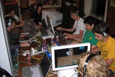 a group of people sitting at a table with laptops and headphones in front of them