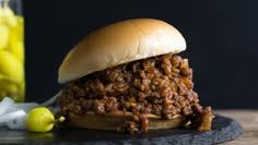 a sloppy joe sandwich sitting on top of a black plate next to some pickles