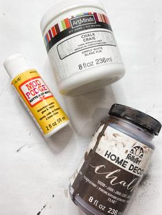 two jars of acrylic paint and one jar of glue sitting on the floor